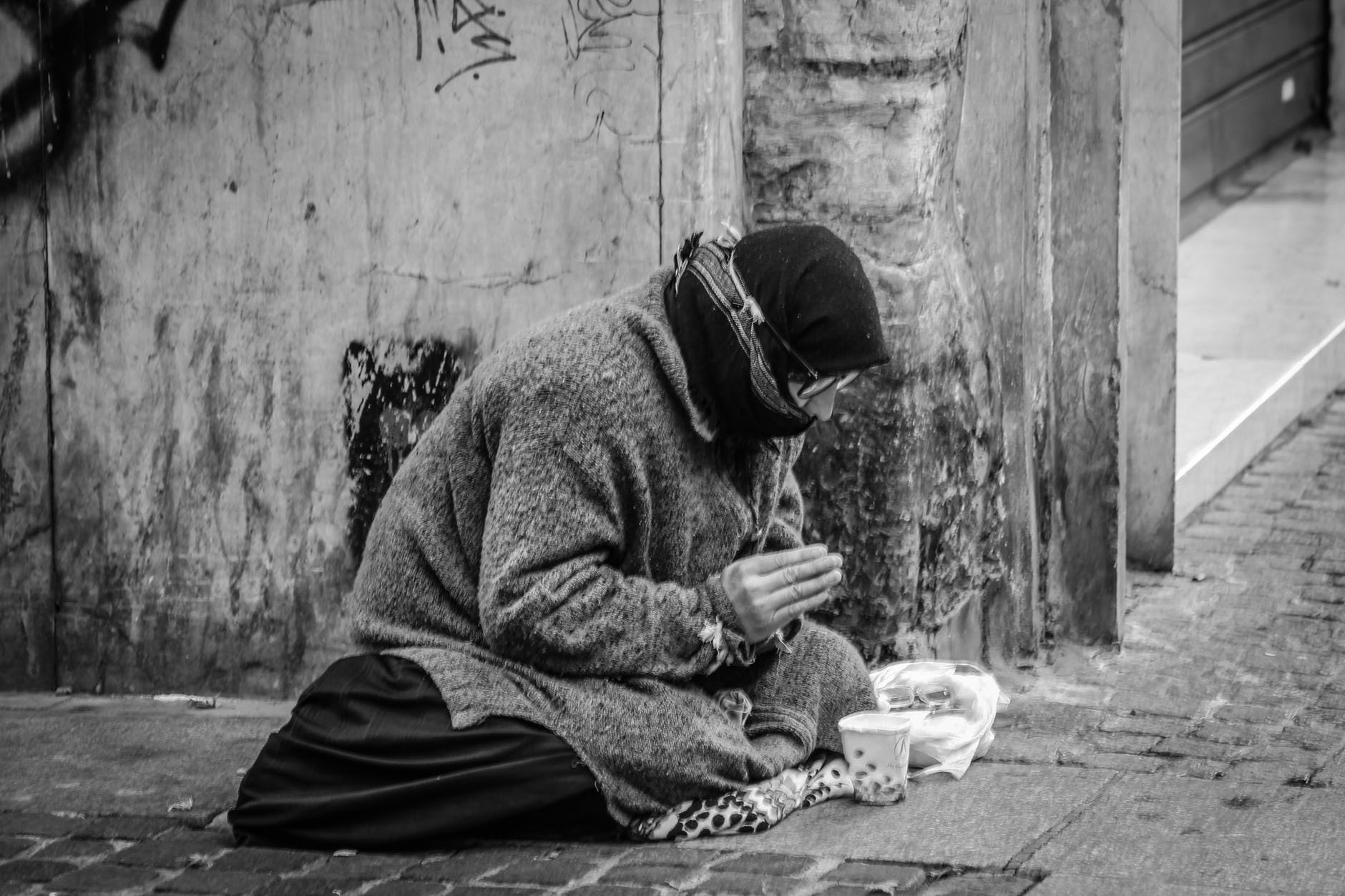 grayscale photography of man praying on sidewalk with food in front